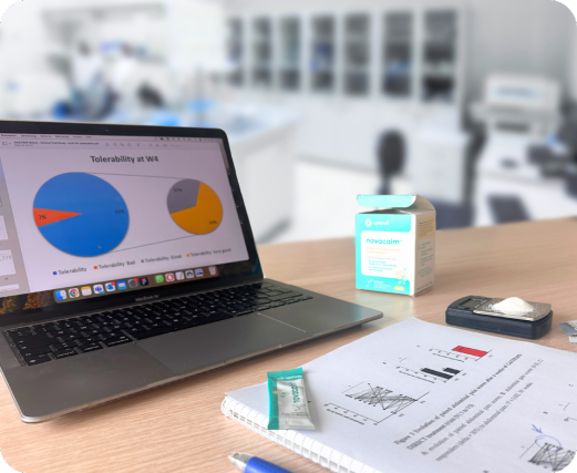 Produktbild – Ein kleiner Karton mit der Aufschrift „novacalm“ steht auf einem Schreibtisch neben einem Laptop, auf dessen Bildschirm ein Tortendiagramm mit dem Titel „Tolerability at W4“ zu sehen ist.