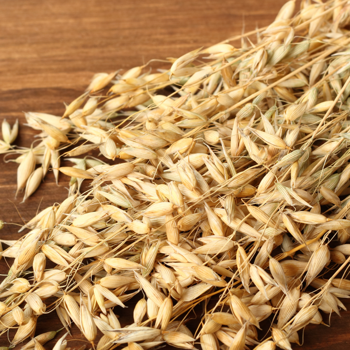 Produktbild – Ein Haufen Haferähren liegt auf einer dunklen Holzoberfläche.