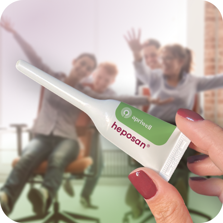 Eine Hand hält eine kleine weiße Tube mit grünem Etikett, auf dem "apriwell" und "heposan®" steht. Im unscharfen Hintergrund sind fröhliche Menschen zu sehen.