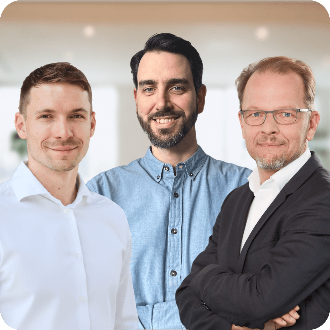 Beratung – Drei freundlich lächelnde Männer stehen als Ansprechpartner zur Verfügung. Links ein Mann in einem weißen Hemd, in der Mitte ein Mann mit Bart in einem blauen Hemd und rechts ein Mann mit Brille und Bart in einem dunklen Sakko über einem weißen Hemd.