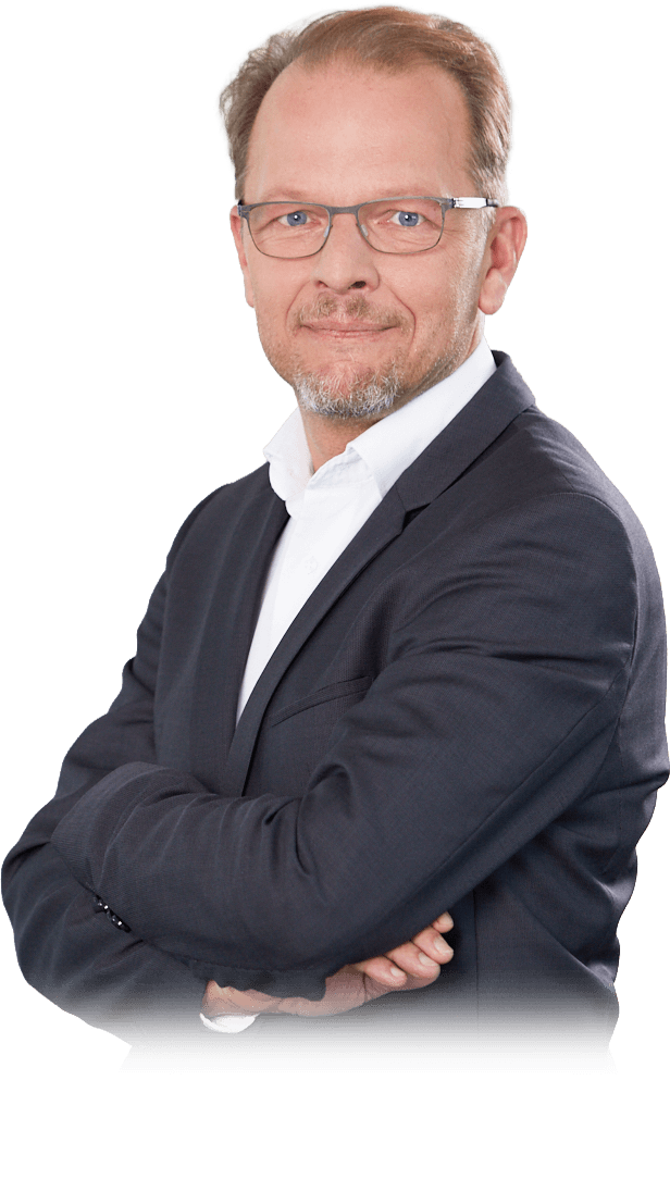 Ein lächelnder Mann mit Brille und grau meliertem Bart in einem dunkelgrauen Anzug und weißem Hemd. Seine Arme sind vor der Brust verschränkt.