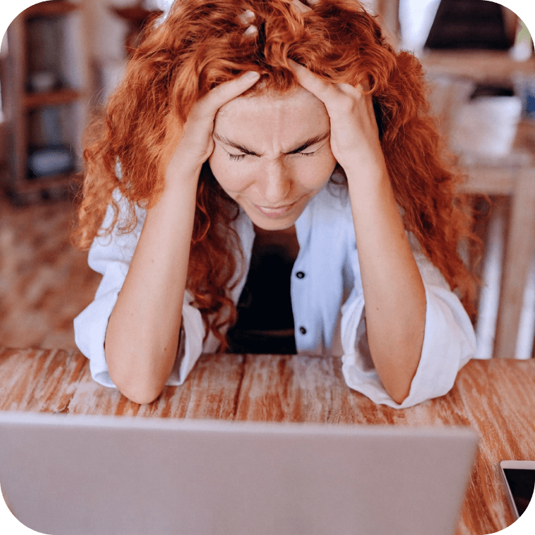 Illustration: Eine Person mit langen, roten Locken sitzt an einem Tisch vor einem Laptop und hält sich mit geschlossenen Augen die Hände an den Kopf.