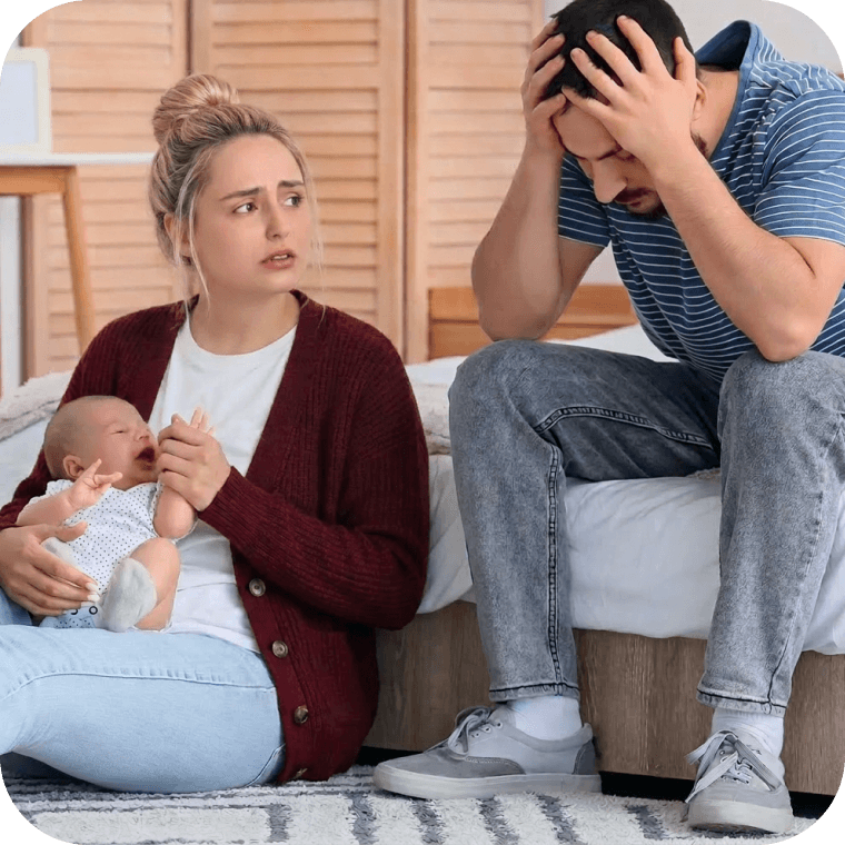 Illustration: Eine Frau und ein Mann sitzen erschöpft auf dem Boden vor einem Bett. Die Frau hält ein weinendes Baby im Arm und blickt besorgt. Der Mann hat den Kopf in seine Hände gestützt und wirkt sichtlich belastet. Die Szene verdeutlicht eine stressige und überfordernde Situation im Alltag.