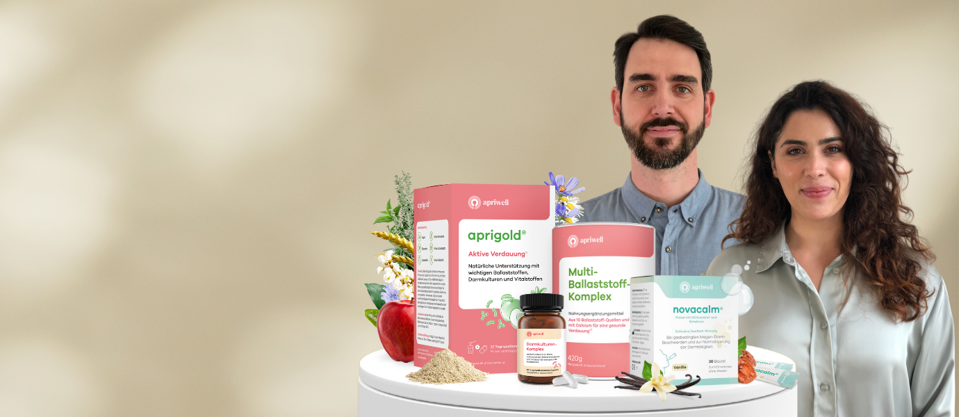 Beratung – Ein Mann und eine Frau stehen lächelnd hinter mehreren Produkten: aprigold zur aktiven Verdauung, Multi-Ballaststoff-Komplex und novacalm.